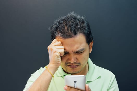 Asian man 40s have a short hair in polo shirt strain have a unhappy gesture with failure and problems concept using smartphone on black background dark style