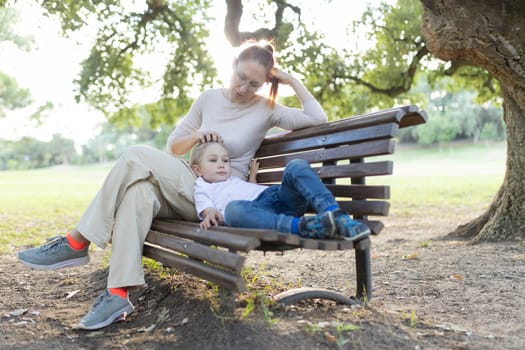 Mother is listening to her son while sitting on a bench in a park