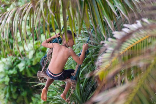 Asian young boy swinging on a rope swing at a beach