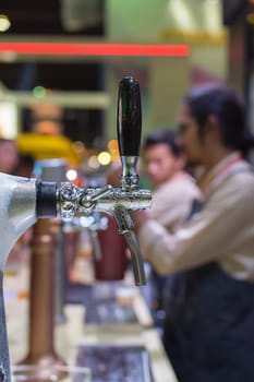 Barman or bartender pouring a draught lager beer from beer tap on counter for serving in a restaurant or pub.
