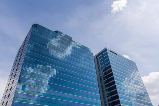 Exterior of glass office building reflection with blue sky and white cloud in a city with business, finance, construction and global warming concept