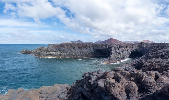 Volcanic coastline with rugged rocks and ocean under a partly cloudy sky.