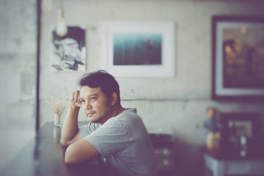Asian man 40s in gray t-shirt have a happy and think gesture in a coffee shop cafe