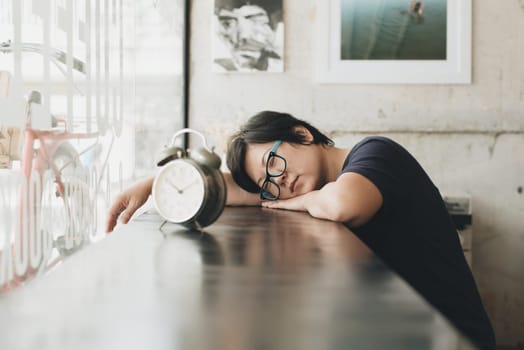 Asian women 40s white skin in black t-shirt with eye glasses sleep for relax or tired between waiting something in a coffee shop cafe with a clock vintage style