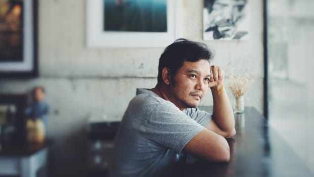 Asian man 40s in gray t-shirt have a happy and think gesture in a coffee shop cafe