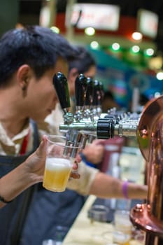 Barman or bartender pouring a draught lager beer from beer tap on counter for serving in a restaurant or pub.