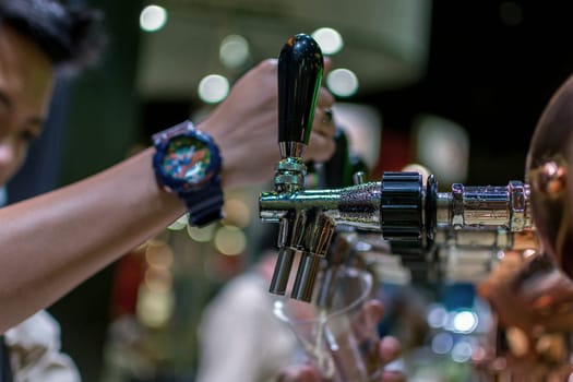 Barman or bartender pouring a draught lager beer from beer tap on counter for serving in a restaurant or pub.