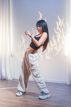 A young woman performs a dynamic dance in a well-lit studio, showcasing her skills and passion. The flames projected on the wall add an artistic touch to her movements.