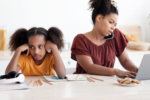 Angry african american teen girl sitting by working mom, need for attention, kitchen interior. Busy black lady working from home, using laptop and having phone conversation, have no time for kid