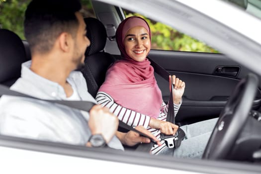 Smiling millennial middle eastern lady in hijab and male fasten seat belts, enjoy travel in car, copy space. Road trip with family, safety and life insurance, journey together at summer vacation