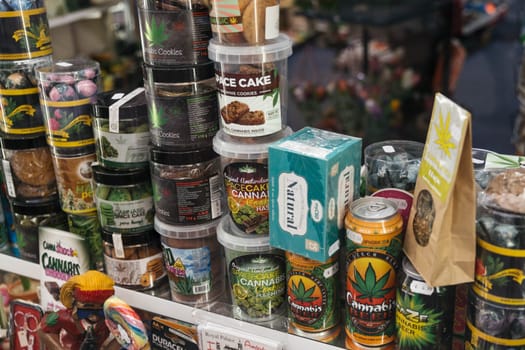 AMSTERDAM, THE NETHERLANDS - APRIL 15, 2019: Shop showcase window with cookies, candies, drinks, jars of cannabis as a souvenir in the store