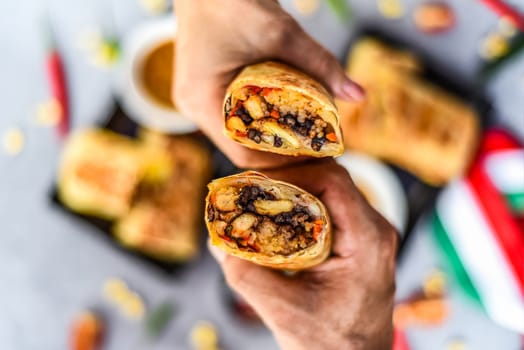 Hands holding Mexican burritos with chicken, rice, beans,cheese served with sauce borracha