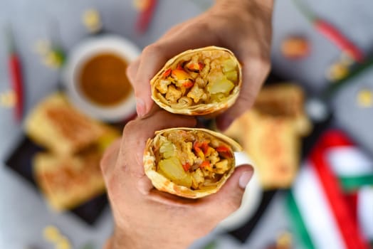 Hands holding vegetarian Mexican burritos with potato, tofu,rice served with sauce borracha