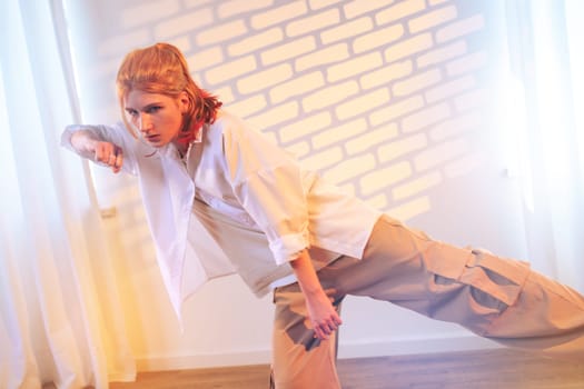 A young model strikes a dramatic pose wearing casual streetwear in a studio. Soft lighting creates a warm atmosphere, highlighting the unique wall design and the model's confident expression.