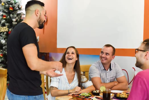 Three friends eating mexican food in a cafe and talking to mexican man waiter
