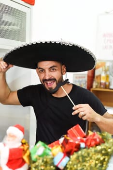 Mexican man in sombrero holding mustache on a stick and smiles in the camera