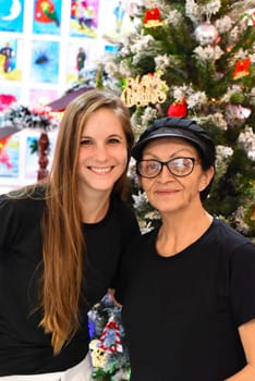 Young slovak woman hugging with senior mexican woman standing together against christmas tree