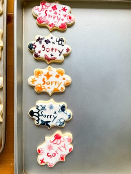 A set of five beautifully decorated sugar cookies each featuring the word sorry written in colorful icing The cookies are placed on a baking sheet and have intricate hand-drawn designs in red blue orange and black icing A creative and thoughtful way to express an apology through homemade treats