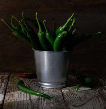 Vibrant green chilies emerge from a metallic bucket, creating a rustic charm against the weathered wooden backdrop.