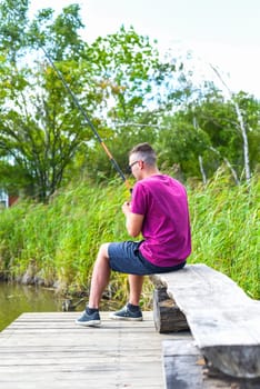 Young fisherman sitting on wooden pier, fishing in the lake. he holding the rod and looking at float