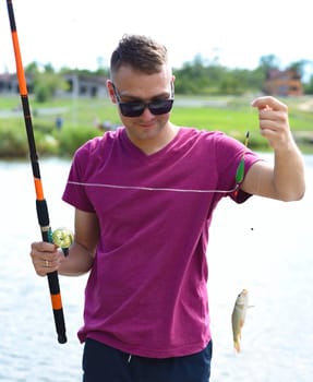 Young fisherman holding crucian carp on fishing rod against a pond