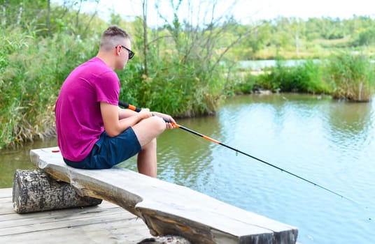 Young fisherman sitting on wooden pier, fishing in the lake. he holding the rod and looking at float