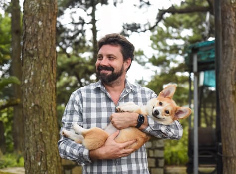 Happy bearded man holding his welsh corgi dog and smiles
