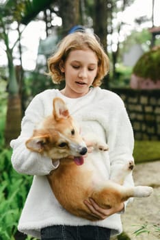 Little cute girl holding her corgi dog on an autumn day