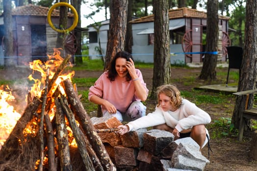 Mother with her daughters spending time together, kindle a fire and throw sticks
