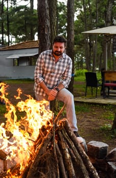 Bearded man making a bonfire in camping in the pine forest at night