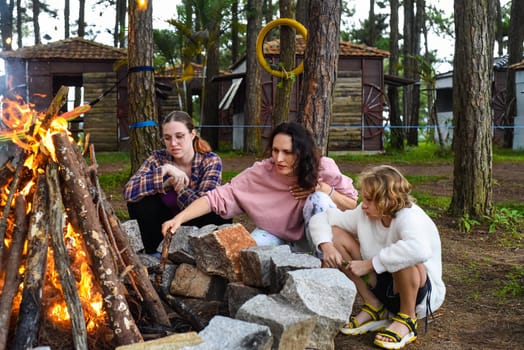 Mother with her daughters spending time together, kindle a fire and throw sticksMother with her daughters spending time together, kindle a fire and throw sticks
