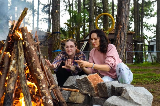 Mother with her daughters spending time together, kindle a fire and throw sticks