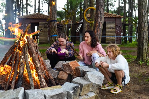 Mother with her daughters spending time together, kindle a fire and throw sticksMother with her daughters spending time together, kindle a fire and throw sticks