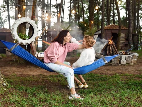 Mother and her daughter fooling around and sitting in hammock in the eveningMother and her daughter fooling around and sitting in hammock in the evening