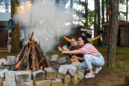 Mother with her daughters spending time together, kindle a fire and throw sticks