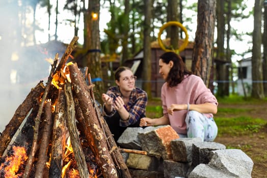 Mother with her daughters spending time together, kindle a fire and throw sticks