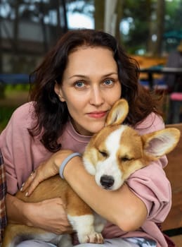 Portrait of beautiful young brunette woman holding her corgi dog and looking at camera