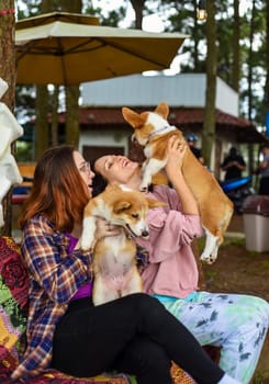 mother with her daughter hugging their corgi dogs in the garden