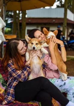mother with her daughter hugging their corgi dogs in the garden