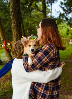 Cozy sisters holding their smiling welsh corgi dog