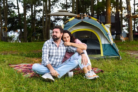 Young married couple sitting in the forest near tent and looking at sunset