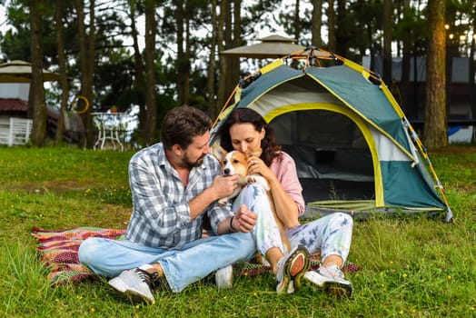 Young married couple with their corgi dog sitting in the forest near tent and looking at sunsetYoung married couple with their corgi dog sitting in the forest near tent and looking at sunset