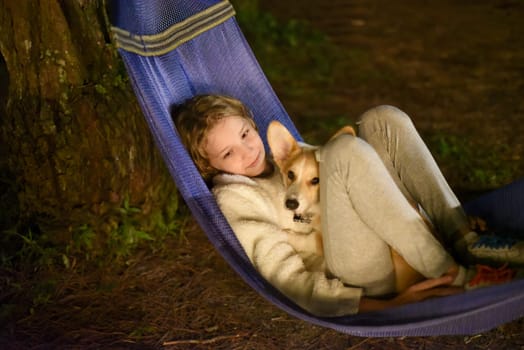 Cute little girl child sleeping in hammock and holding a corgi dog together in camping trip