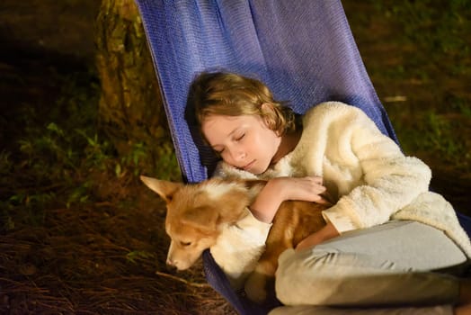 Cute little girl child sleeping in hammock and holding a corgi dog together in camping trip