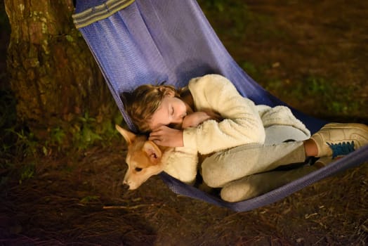 Cute little girl child sleeping in hammock and holding a corgi dog together in camping trip