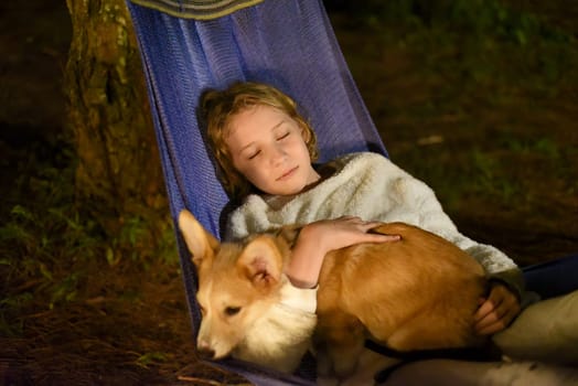 Cute little girl child sleeping in hammock and holding a corgi dog together in camping trip