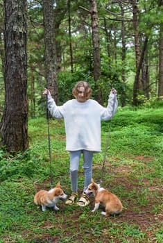 Little kid girl walking with her corgi dogs in the forest