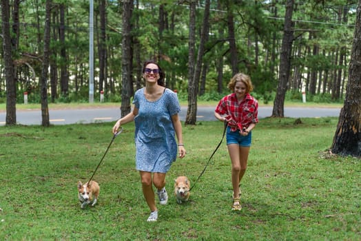 Mother and her daughter running with her corgi dogs in the forest