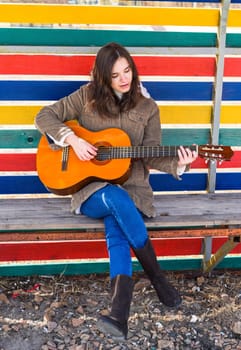Young woman playing guitar and laughing, sitting on a bench against colorful background