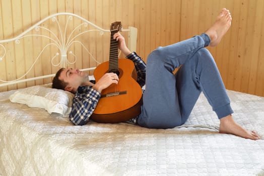 Young man playing guitar and laying on bed on weekend morning